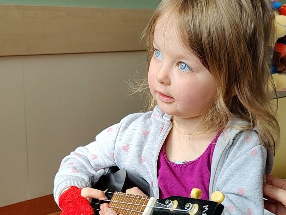 Leandra mit ihrer Spielzeuggitarre. Sie möchte gerne wieder andere Kinder treffen und gesund sein.