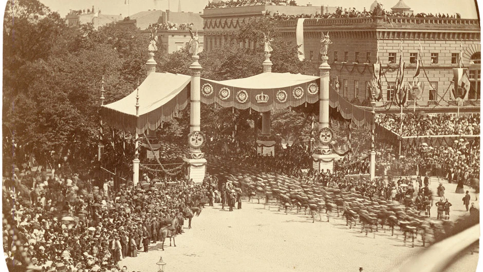 Der pompöse Einmarsch des siegreichen preußischen Heeres und seiner Verbündeten in die Kaiser- und Reichshauptstadt Berlin fand am 16. Juni 1871 statt. Hier ziehen die Truppen unter dem Ehrenbaldach vom Pariser Platz in Richtung Unter den Linden. Das Gebäude ist das Palais Redern. Dort steht jetzt das Adlon.
