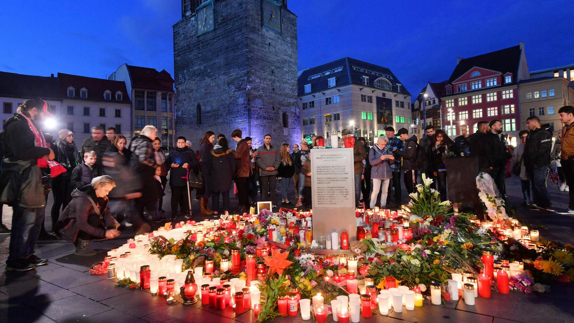 Menschen stehen in der Abenddämmerung auf dem Marktplatz neben Blumen und Kerzen, um ein Zeichen gegen Gewalt zu setzen und um zu Trauern. Bei Angriffen mitten in Halle an der Saale in Sachsen-Anhalt sind am 9. Oktober zwei Menschen erschossen worden.