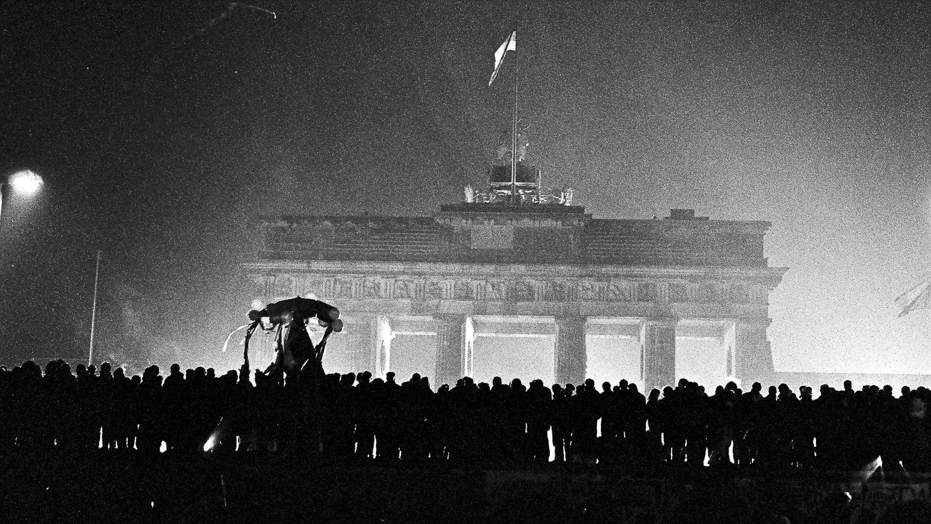 Silvester 1989 am Brandenburger Tor. Berliner aus Ost und West feiern gemeinsam den Jahreswechsel. Hunderte sind auf die Mauer geklettert, die hier so breit ist, dass man darauf stehen kann.