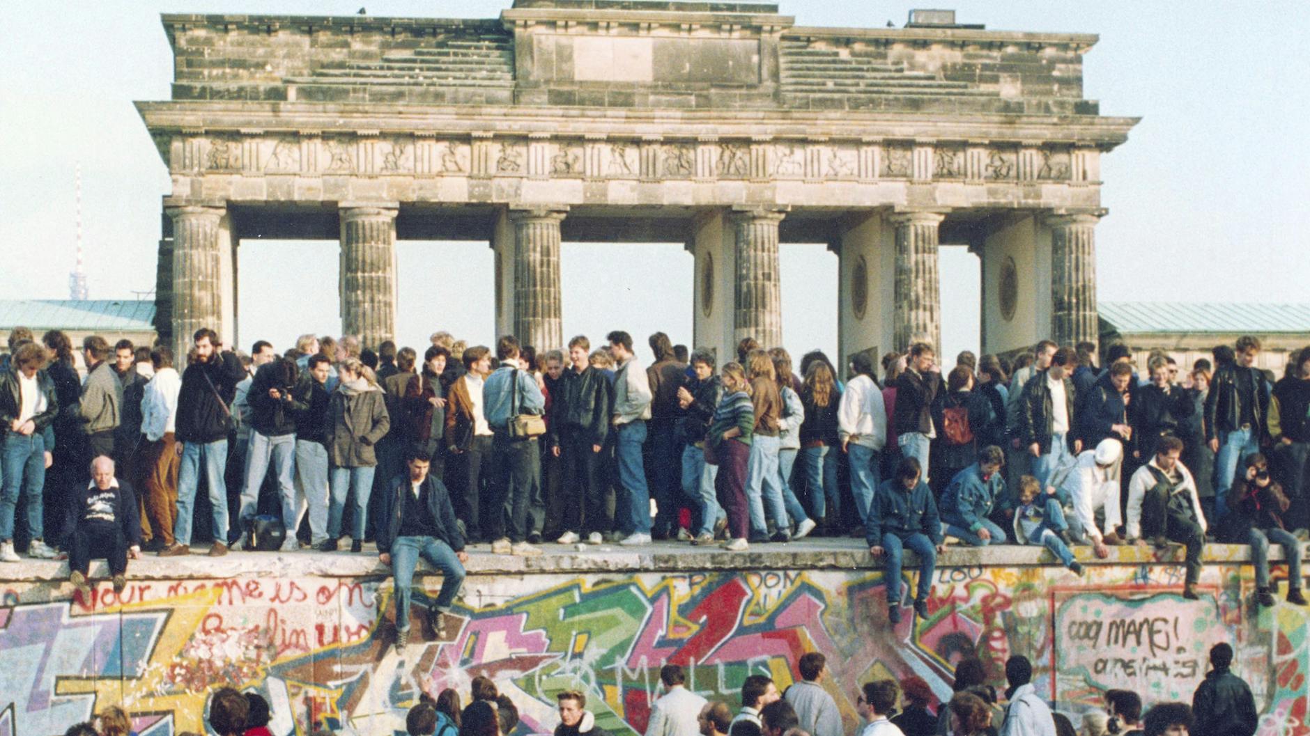 Menschen aus Ost und West stehen gemeinsam auf der Berliner Mauer. 