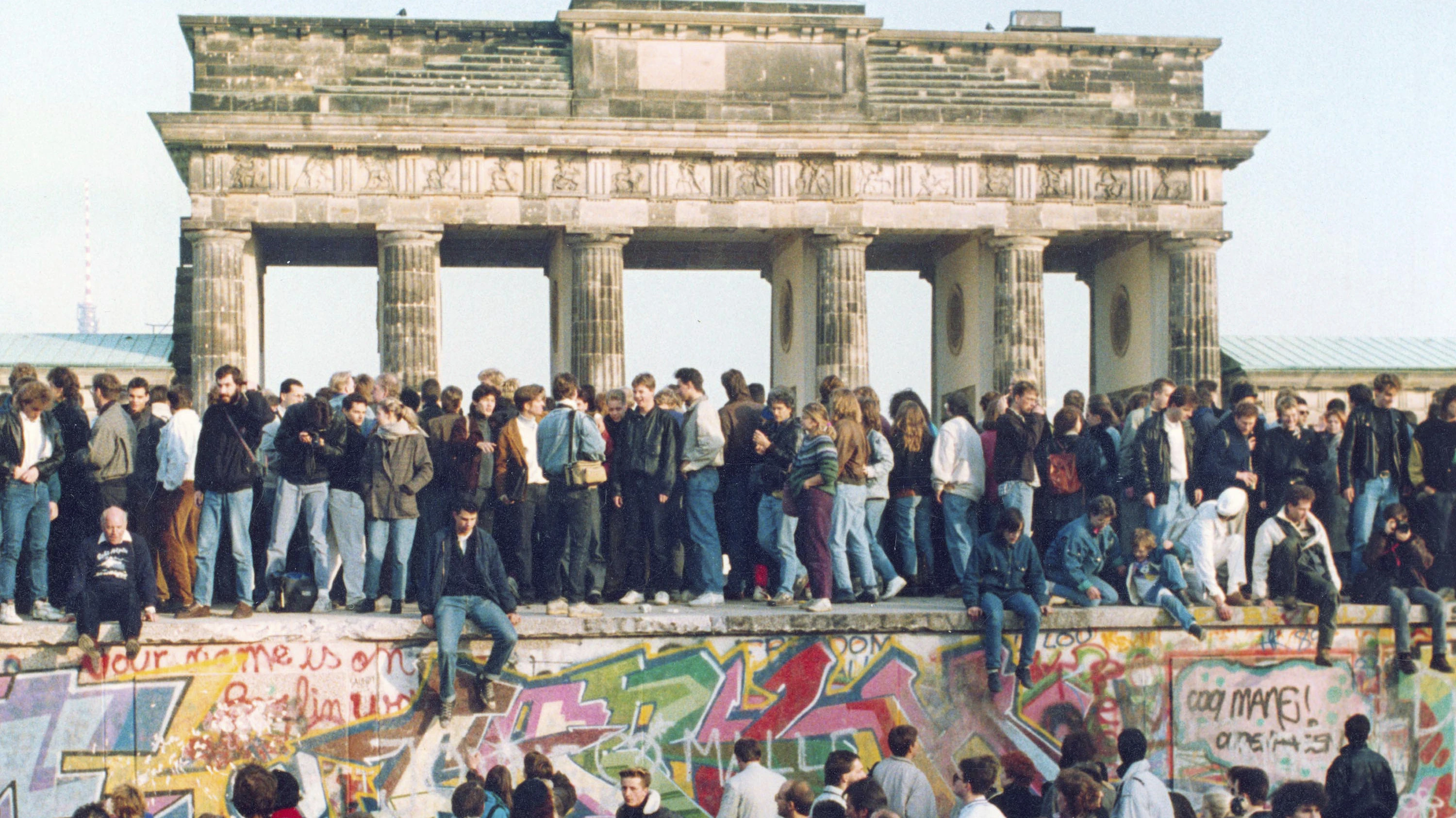 Menschen aus Ost und West stehen gemeinsam auf der Berliner Mauer.&nbsp;