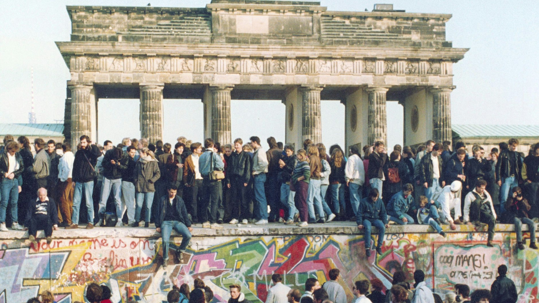 Menschen aus Ost und West stehen gemeinsam auf der Berliner Mauer.&nbsp;