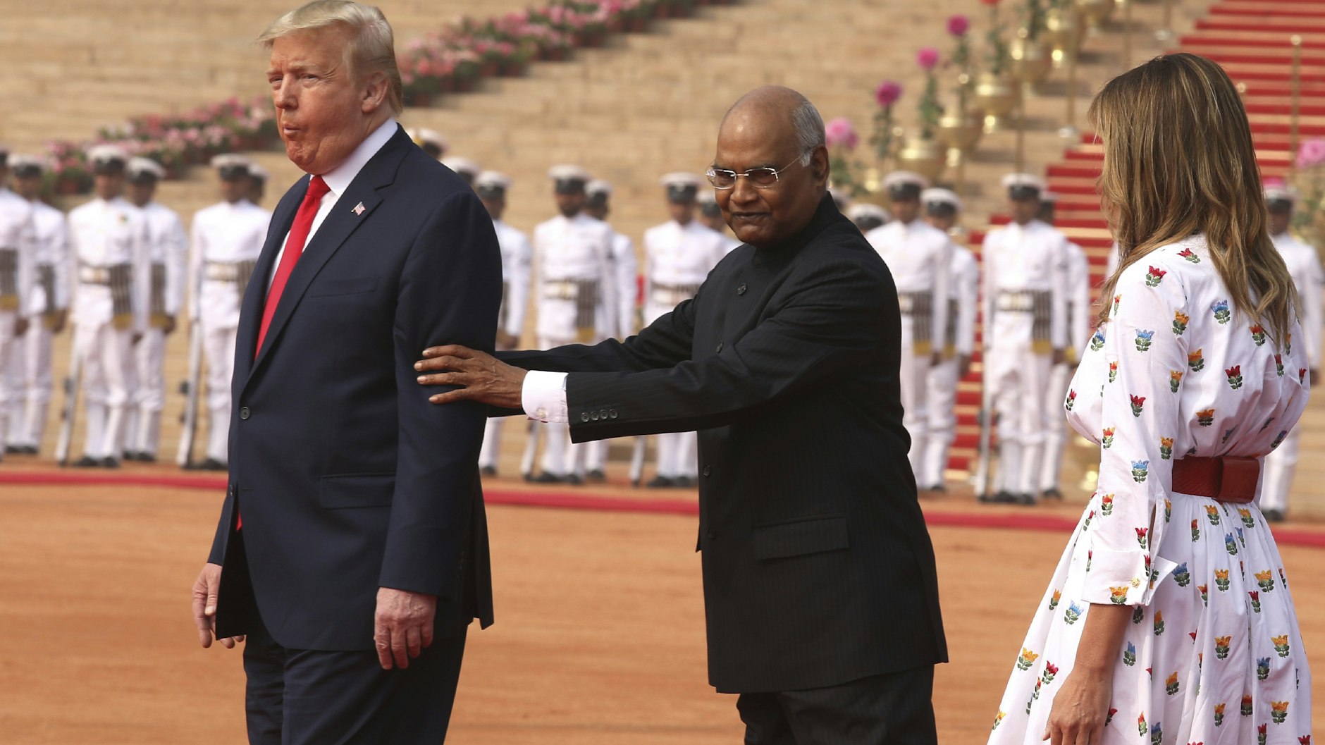Donald Trump (l.) wird von Ram Nath Kovind (m.), Präsident von Indien, positioniert. Melania Trump beobachtet die Szene.