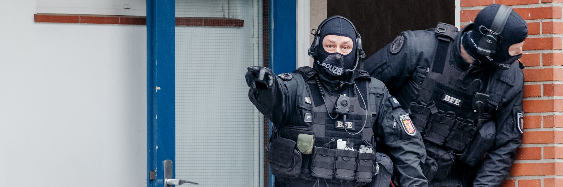 Schwer bewaffnete Polizisten stehen im Rahmen der Razzia vor einem Haus im schleswig-holsteinischen Bad Segeberg.