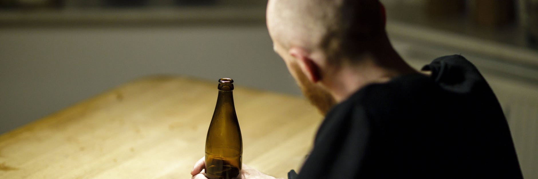 Ein Mann sitzt allein zu Hause an einem Tisch und haelt eine Flasche Bier in der Hand (Symbofoto).