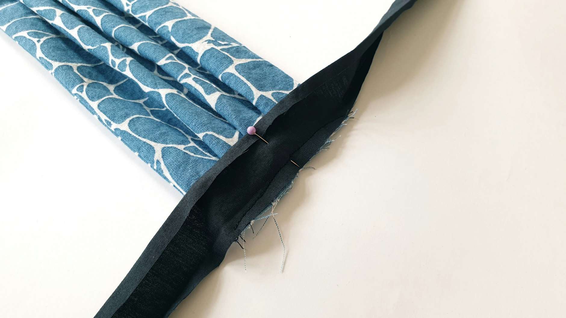 Das Schrägband wird nun aufgeklappt und mit der Nadel auf der Mitte des Mundschutzes befestigt. Mit einer Naht wird das aufgeklappte Schrägband am Mundschutz fixiert.