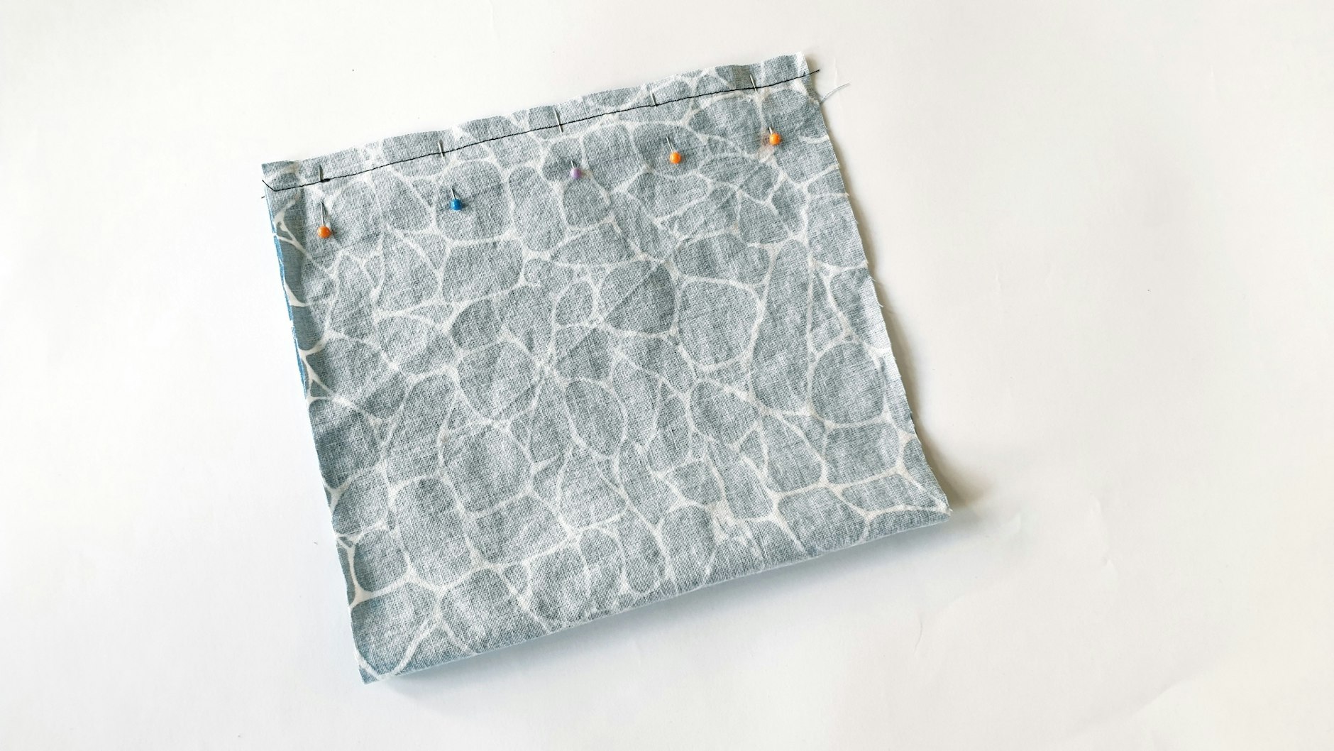 Zuerst faltet man den Stoff so, dass die beiden kurzen Kanten aufeinander liegen. Die schöne Stoffseite, die später außen sein soll, ist jetzt innen. Mit Stecknadeln feststecken und dann zusammennähen.