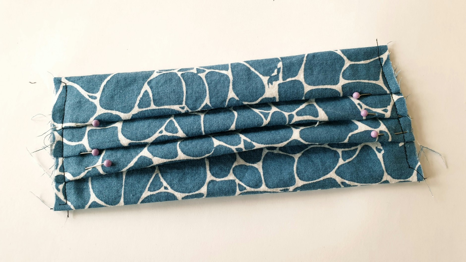 Mit je einer Naht links und rechts fixiert man die Falten nun sicher. Tipp: Stecken die Nadeln waagerecht zur Naht, kann man sie beim Nähen stecken lassen und mit der Nähmaschine drüber nähen.