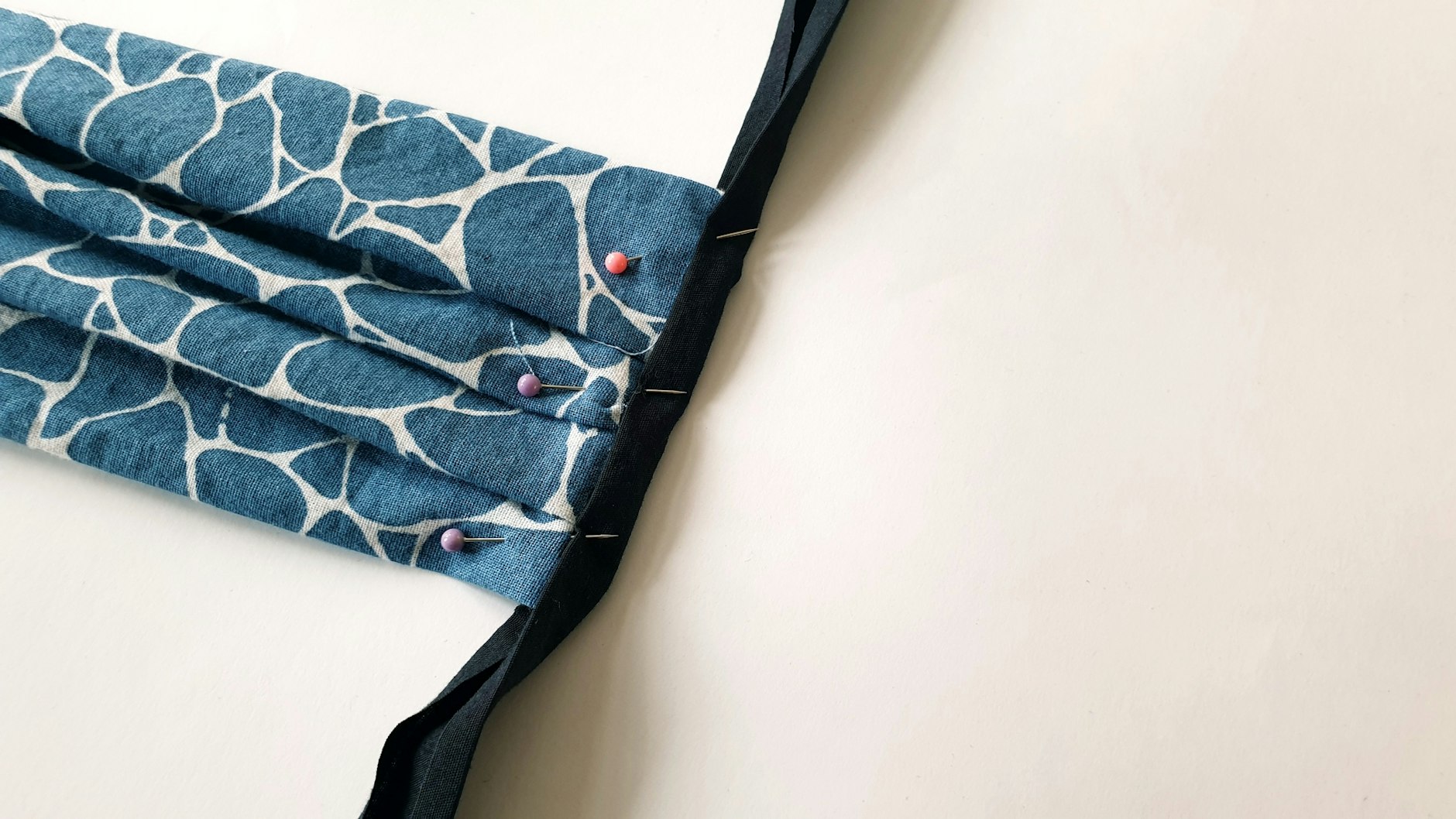 ... und klappt das Schrägband über die offene Kante hinweg in Richtung Mundstück um. Mit Stecknadeln wird das Schrägband nun fixiert.