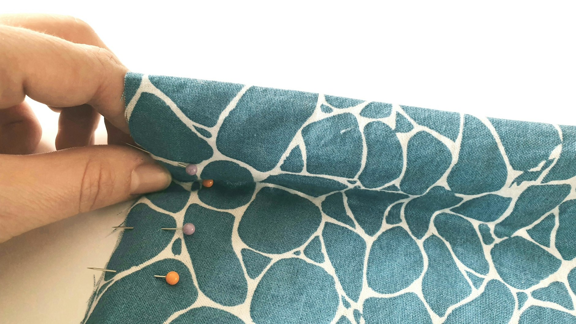 Nun faltet man den Stoff auf Höhe der zweiten Markierung von unten (hier orangefarbene Nadel) nach unten.