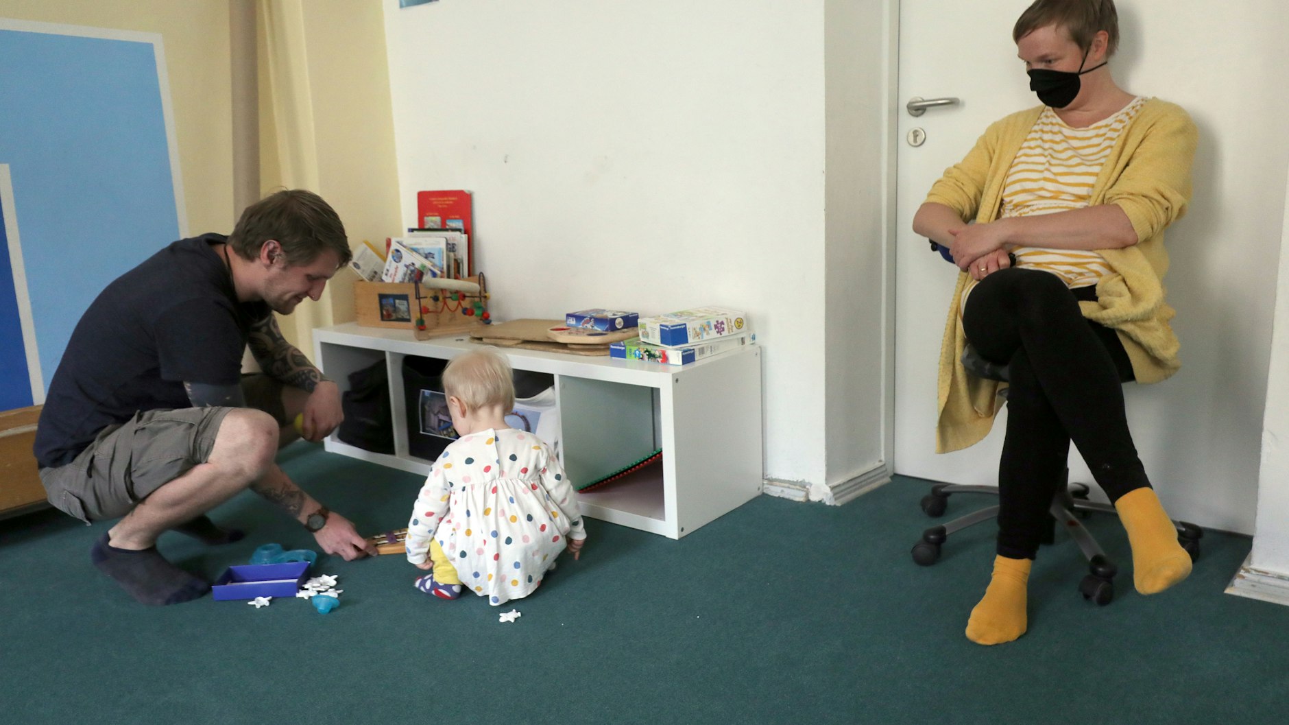 Die Kleine ist zur Eingewöhnung in der Kita, von der Mutter mit Mundschutz beobachtet.