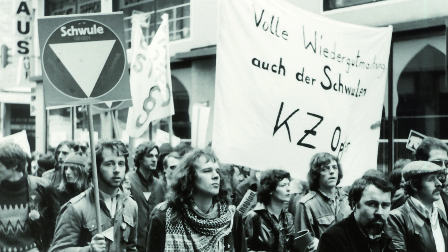 Protestdemonstration für „Volle Wiedergutmachung auch der Schwulen KZ-Opfer“, 1980er-Jahre:&nbsp;Der § 175 des deutschen Strafgesetzbuches, der sexuelle Handlung zwischen Männern unter Strafe stellte, tritt 1872 in Kraft. Im Nationalsozialismus wird er 1935 erheblich verschärft und ausgeweitet. Der entsprechende Paragraph besteht in beiden deutschen Staaten in unterschiedlicher Form noch lange fort. In der Bundesrepublik wird er erst ab 1969 zögerlich und in mehreren Schritten reformiert. Homosexuelle sind deshalb lange Jahre faktisch von Wiedergutmachungszahlungen ausgenommen, da ein entsprechender Antrag einer Selbstanzeige gleich kommt. 1988 wird der § 175 aus dem DDR-Strafgesetzbuch gestrichen, 1994 wird er auch für das Gebiet der alten Bundesrepublik ersatzlos aufgehoben.