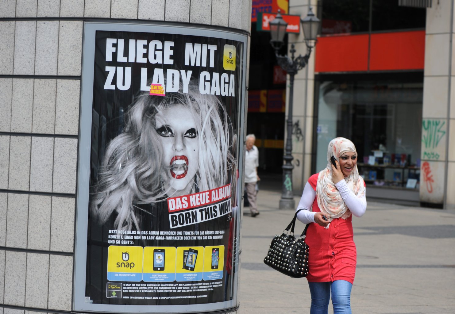 Moderne trifft auf Tradition: Eine junge Frau mit Kopftuch läuft in Neukölln in der Karl-Marx-Straße an einem Lady-Gaga-Plakat vorbei.
