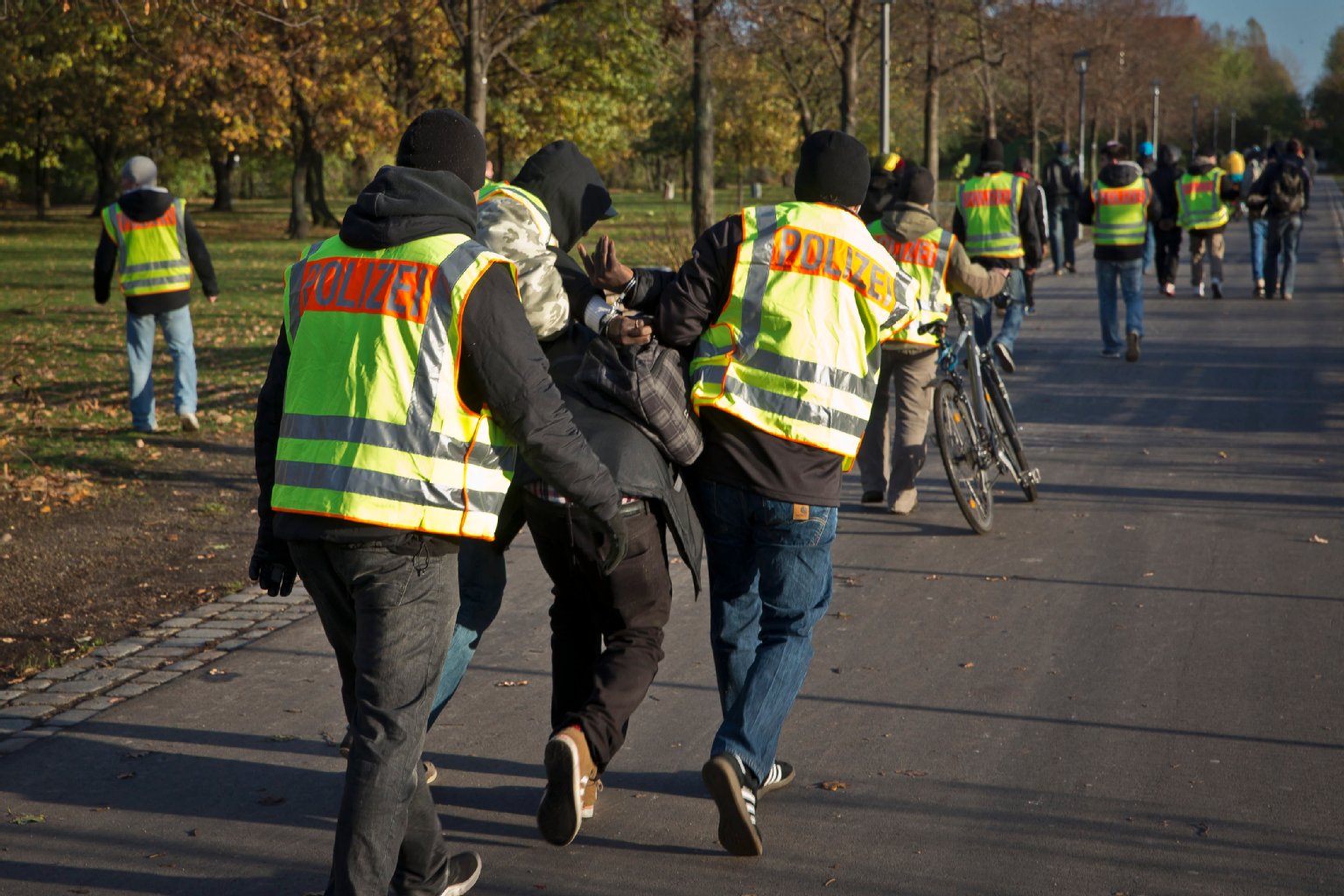 Beamte in gelben Polizei-Westen führen einen Verdächtigen ab.