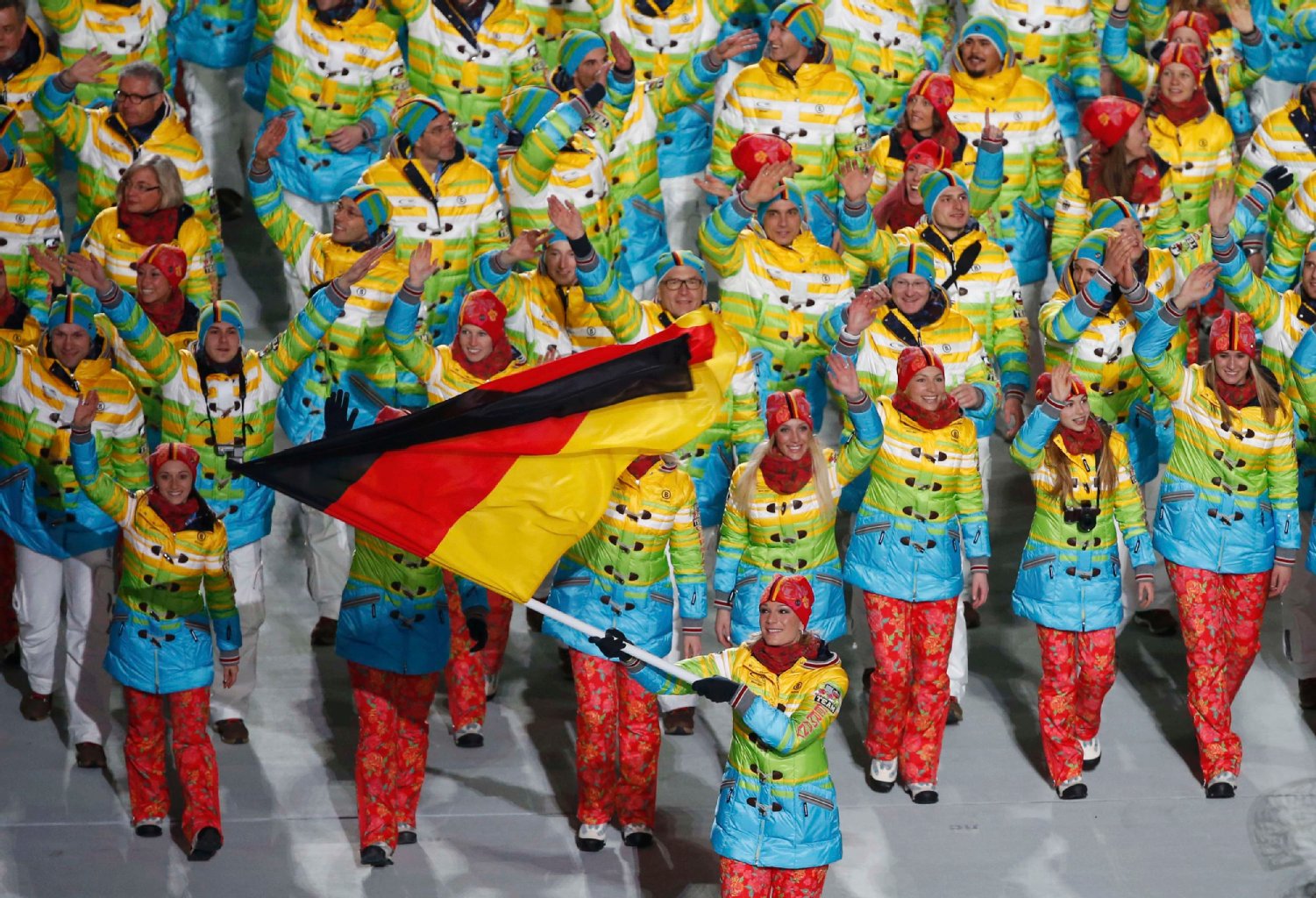 Bekanntheit: Die Skirennnläuferin Maria Höfl-Riesch trägt die Fahne der deutschen Mannschaft ins Stadion. Mit der Nominierung der zweifachen Olympiasiegerin von Vancouver haben sich die Verantwortlichen für die werbewirksamste Figur im Team entschieden. Die durchaus gewöhnungsbedürftige Garderobe der Athleten ist von dem Münchener Modemacher Willy Bogner entworfen worden. Auf jeden Fall heben sich die Sportler gut vom grauweißen Untergrund auf den Skipisten und Eisbahnen des Olympiageländes ab.