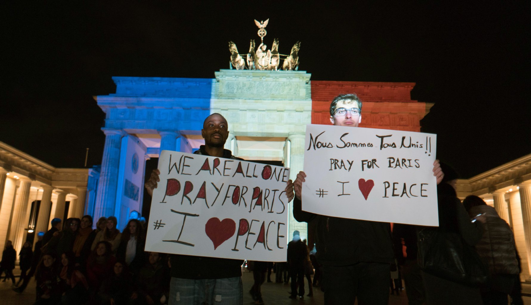 Vor dem Brandenburger Tor halten Menschen Plakate mit Solidaritätsbekundungen für Frankreich.