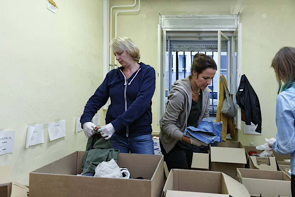 Ehrenamtliche freiwillige Helferinnen sortieren frisch eingetroffenen Kleiderspenden.