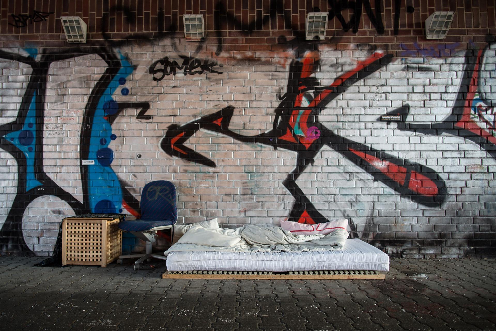 Nachtquartier: Eine leere Matratze, Decken und ein Stuhl unter einer Brücke.
