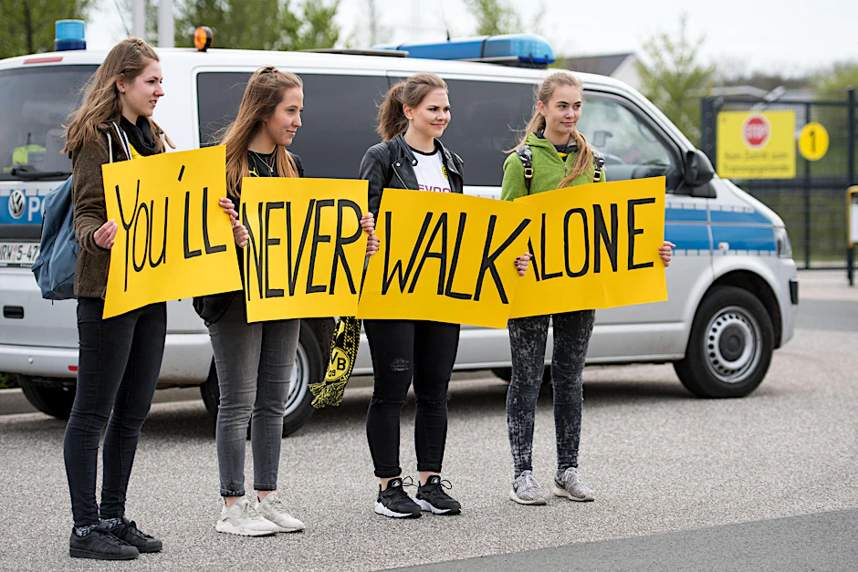BVB-Fans am Mittwoch vor dem Trainingsgelände von Borussia Dortmund. Sie beteuern schriftlich ihre Solidariät. Ein BVB-Profi fährt vorbei.