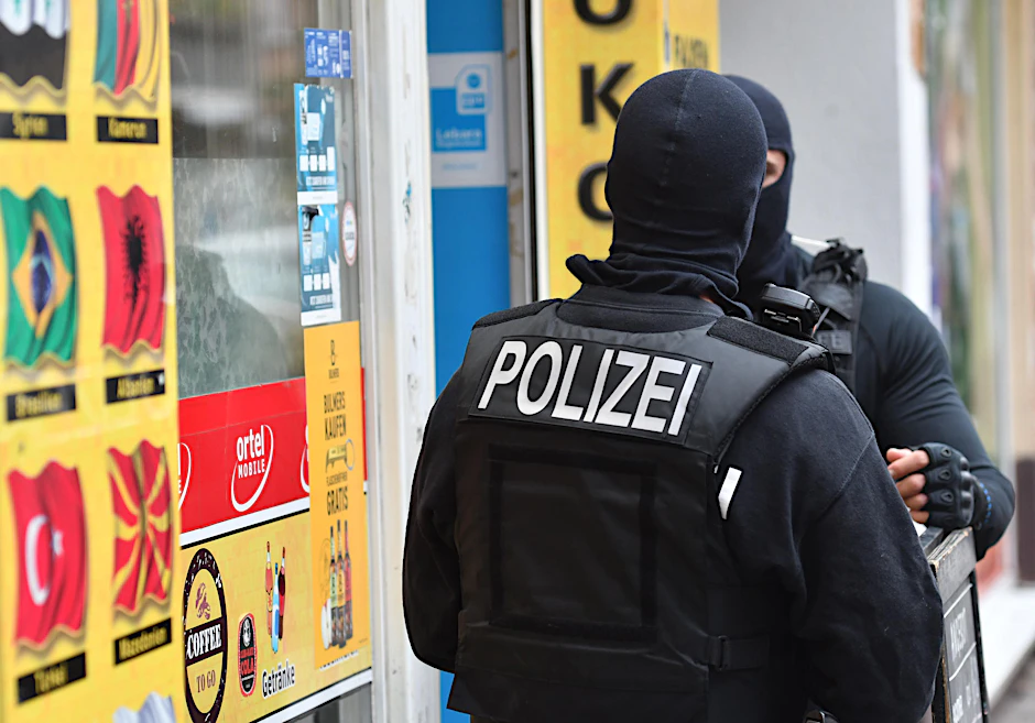 Vermummte Einsatzkräfte stehen vor einem Kiosk im Stadtteil Neukölln. 