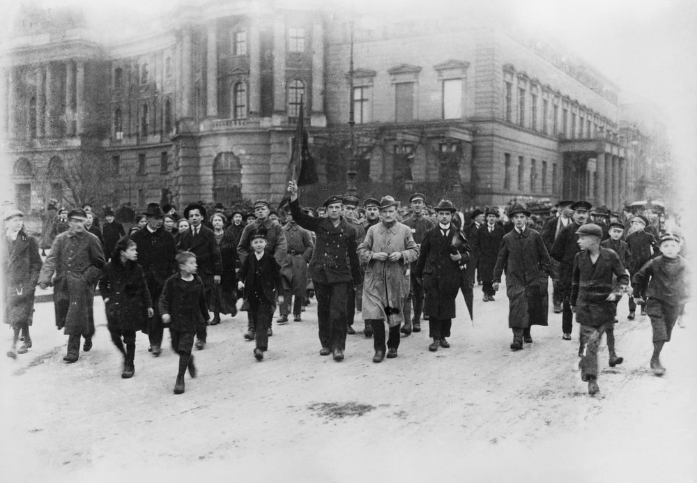Uns nach! Matrosen und Soldaten, Männer, Frauen und Kinder demonstrieren Unter den Linden. Im Hintergrund sind die Alte Bibliothek (links) und das Alte Palais zu sehen.
