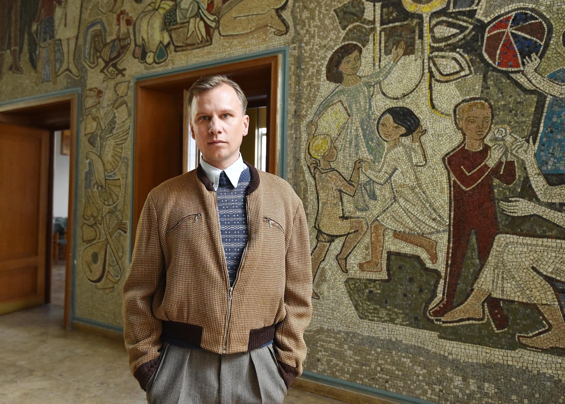 Der Schauspieler Robert Stadlober steht im Rathaus in Eisenhüttenstadt vor dem Natursteinmosaik «Unser neues Leben» von Walter Womacka. 