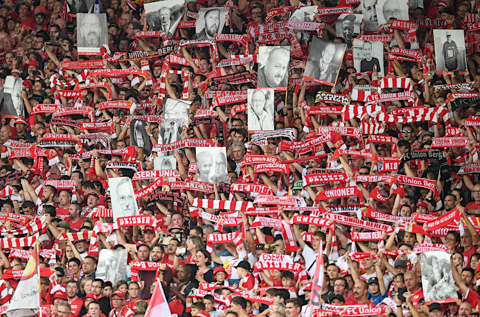 „Endlich dabei“: Union-Fans halten Porträts von Ehemaligen in die Höhe.