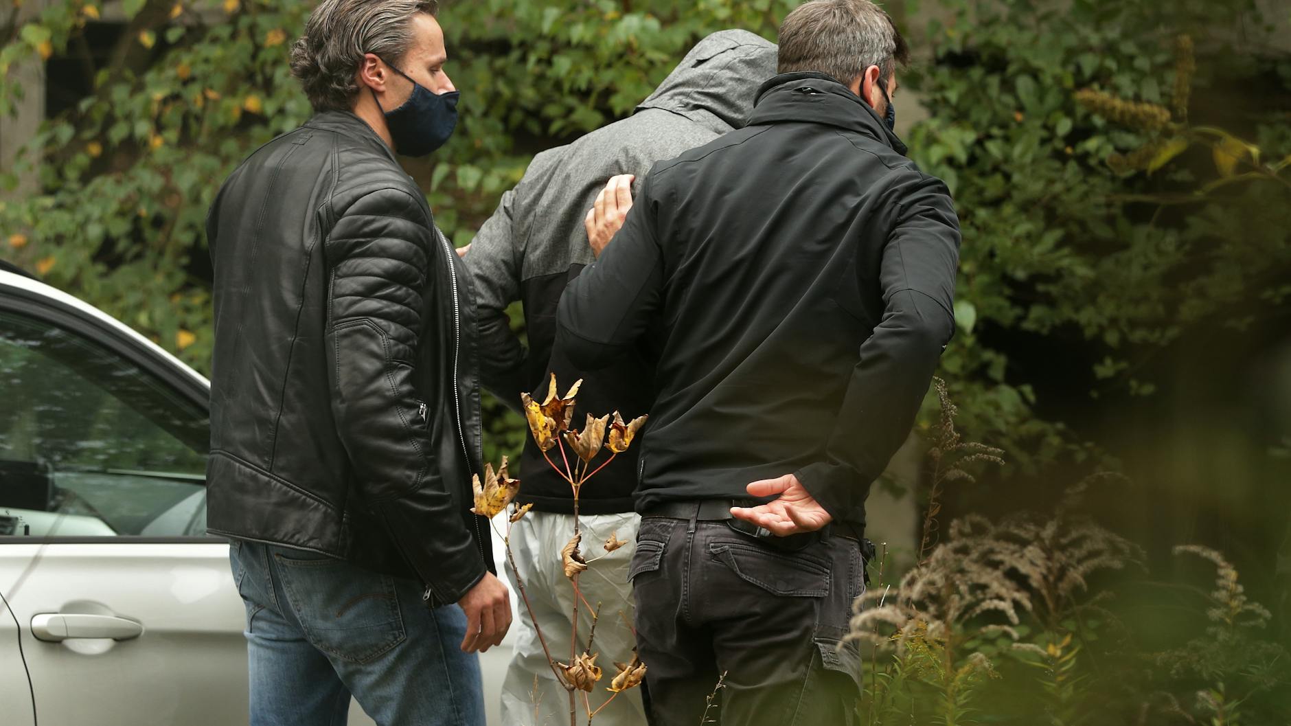 Zwei Polizisten führen einen Tatverdächtigen zum Tatort. 