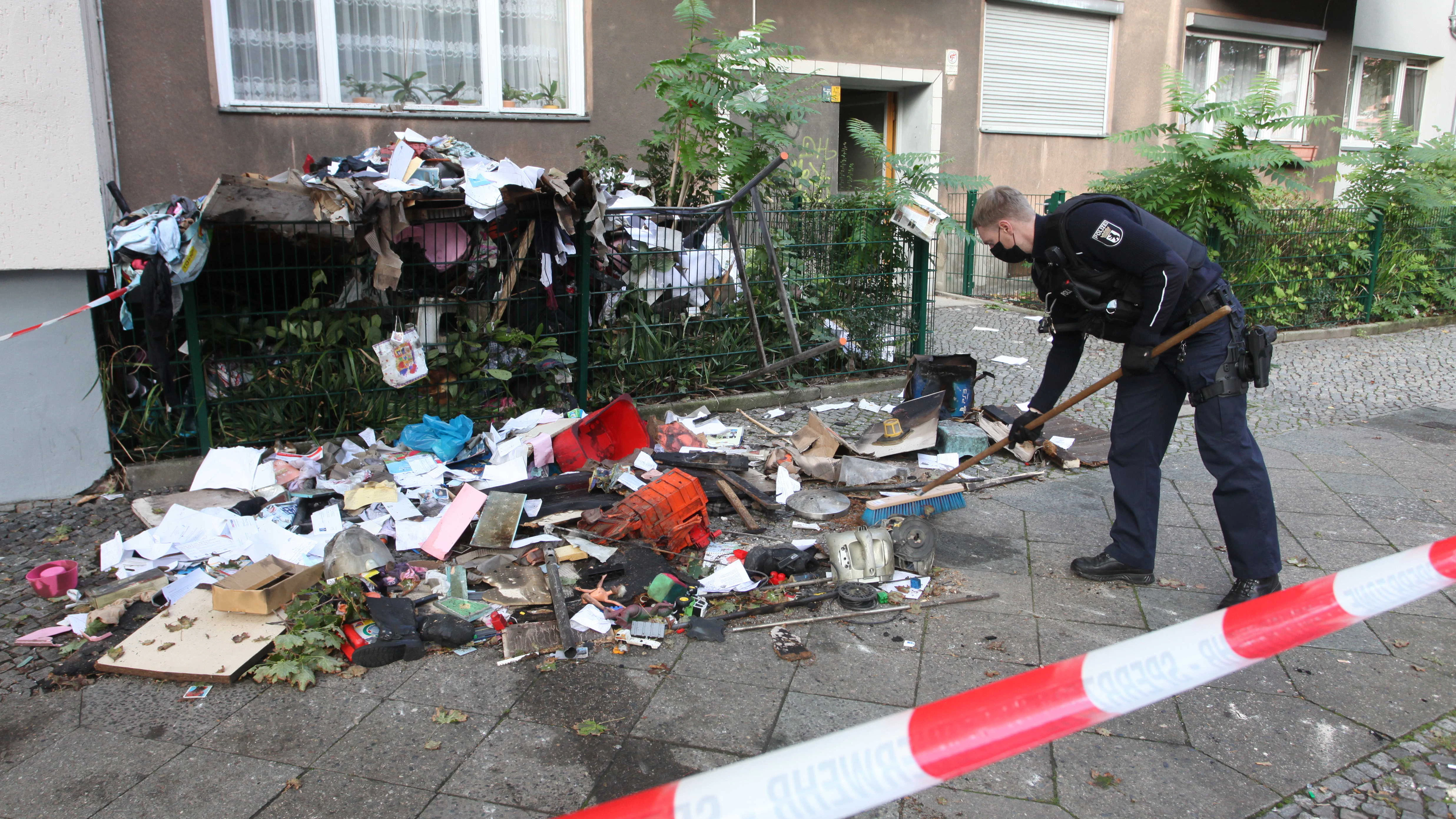 Ein Polizist kehrt vor dem Haus in der Steinmetzstraße die zum Teil verbrannten Sachen der Familie zusammen.&nbsp;