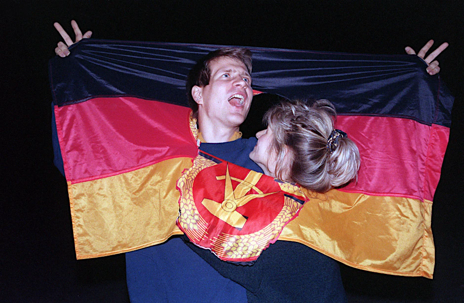 3. Oktober 1990:&nbsp;Ein jubelnden Paar hat sich am Tag der Deutschen Einheit in einer DDR-Fahne dort Platz geschaffen, wo vorher das Emblem Hammer und Zirkel war