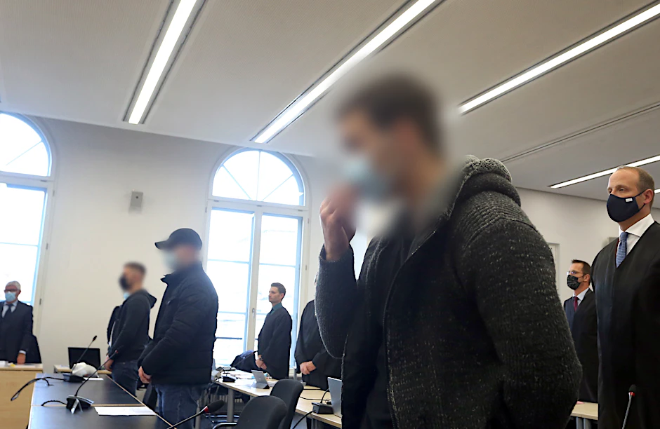 Der Hauptangeklagte (r.) steht neben seinen Mittäter im Gerichtssaal.