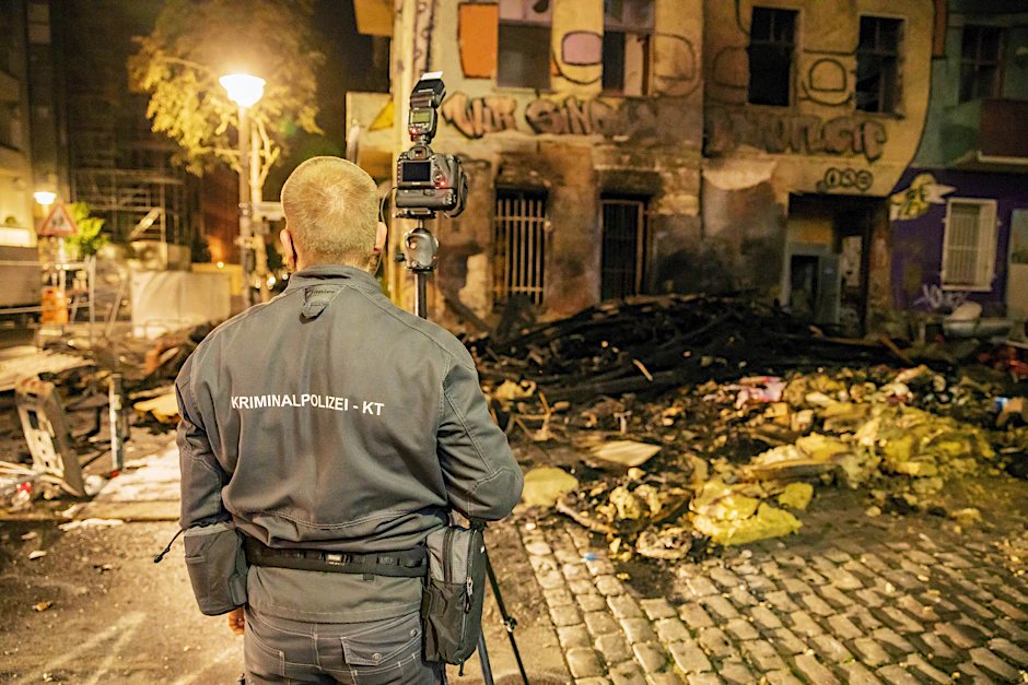 Nach einem Brand vor dem Haus Liebig34 fotografiert ein Polizist die Überreste.