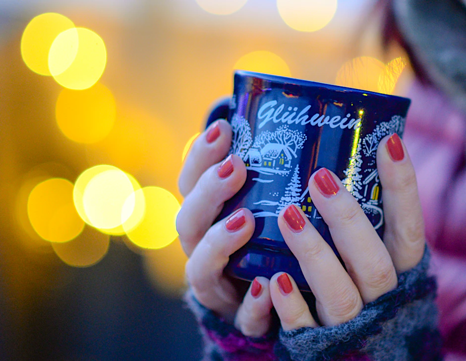 Eine Frau hält auf dem Weihnachtsmarkt eine Tasse mit Glühwein in den Händen.