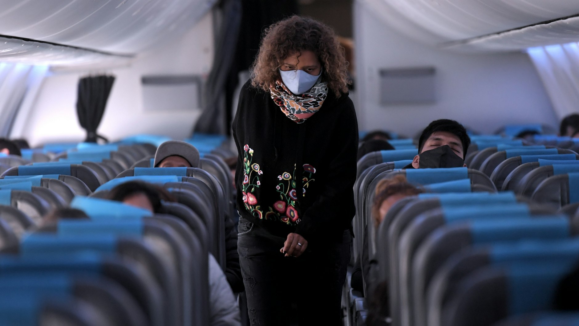 Eine Passagierin mit Mund-Nasen-Schutz sucht nach ihrem Sitzplatz in einem Flugzeug.
