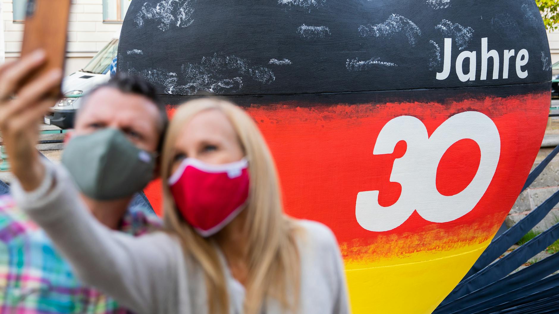 Ein Pärchen fotografiert sich in Potsdam vor einem schwarz-rot-goldenen Herz mit der Aufschrift „30 Jahre“.