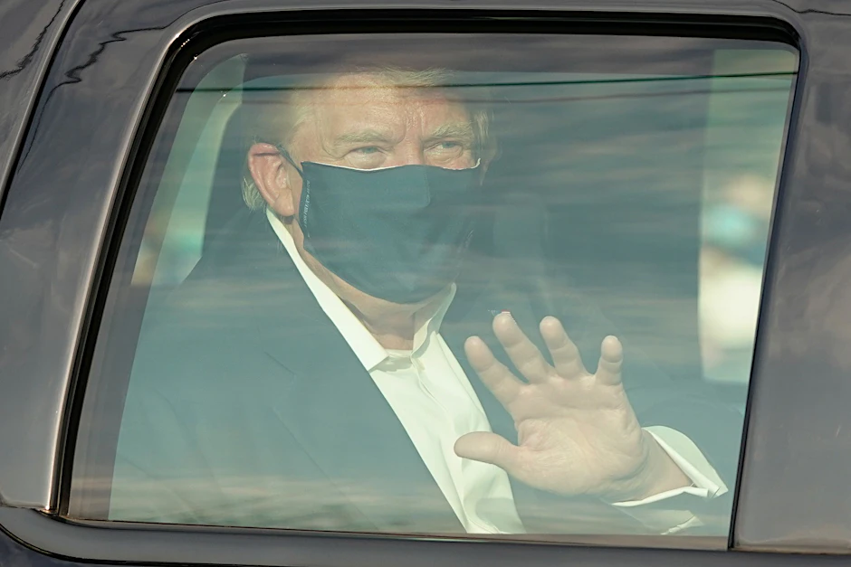 Präsident Donald Trump lässt sich von Bodyguards herumkutschieren, winkt seinen wartenden Fans aus dem Auto zu.