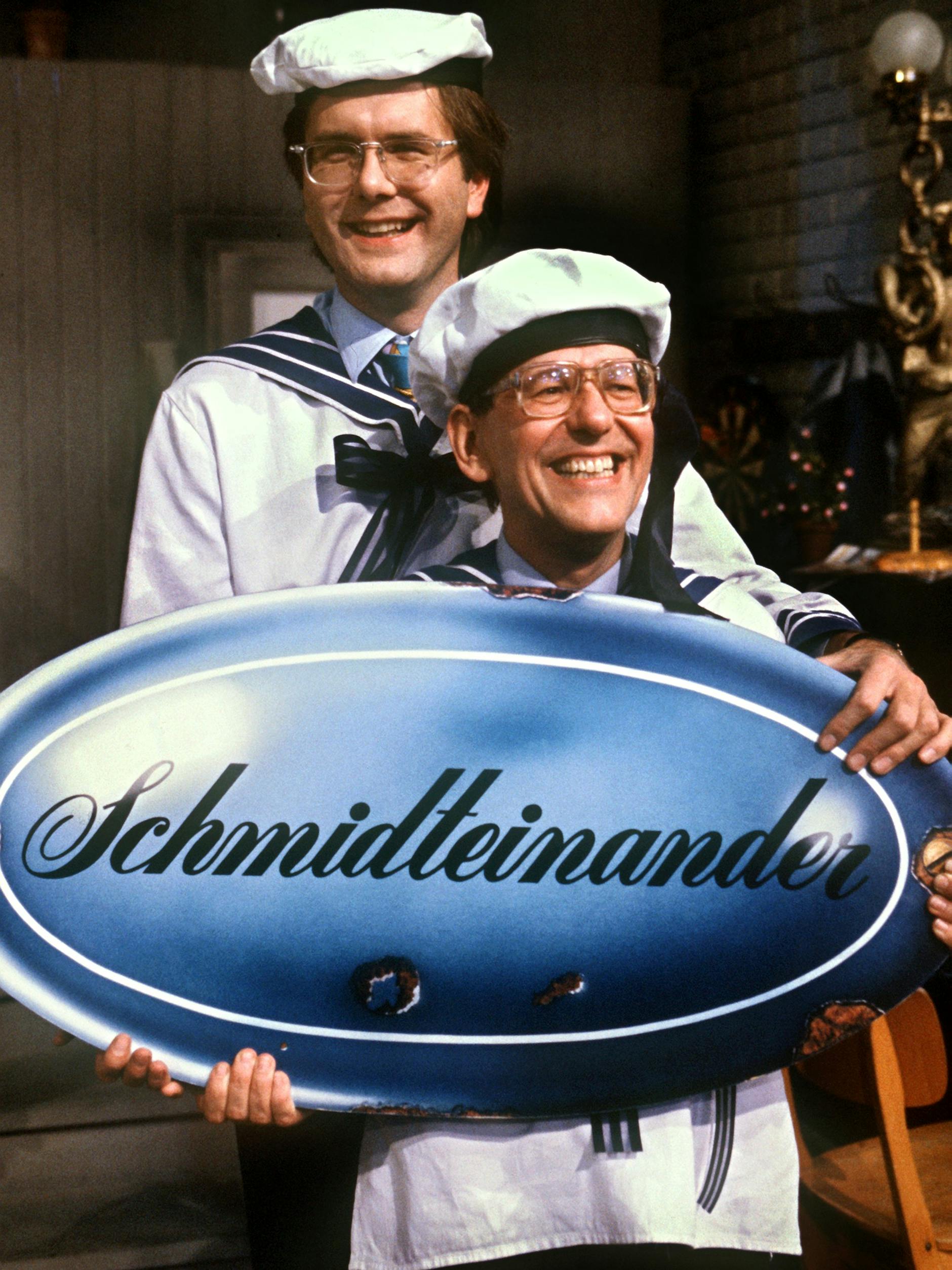 Die Entertainer Herbert Feuerstein (unten) und Harald Schmidt präsentieren 1991 das Logo ihrer gemeinsamen TV-Show „Schmidteinander“.