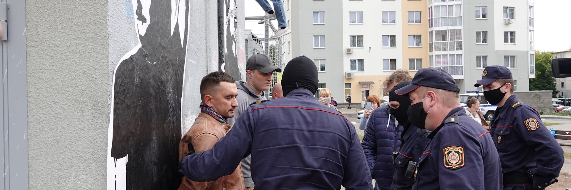Stepan Latypow (links) stellt sich in seinem Minsker Wohnviertel maskierten Polizisten entgegen. Sie nehmen ihn wegen der Bilder oppositioneller DJs an der Wand fest. 