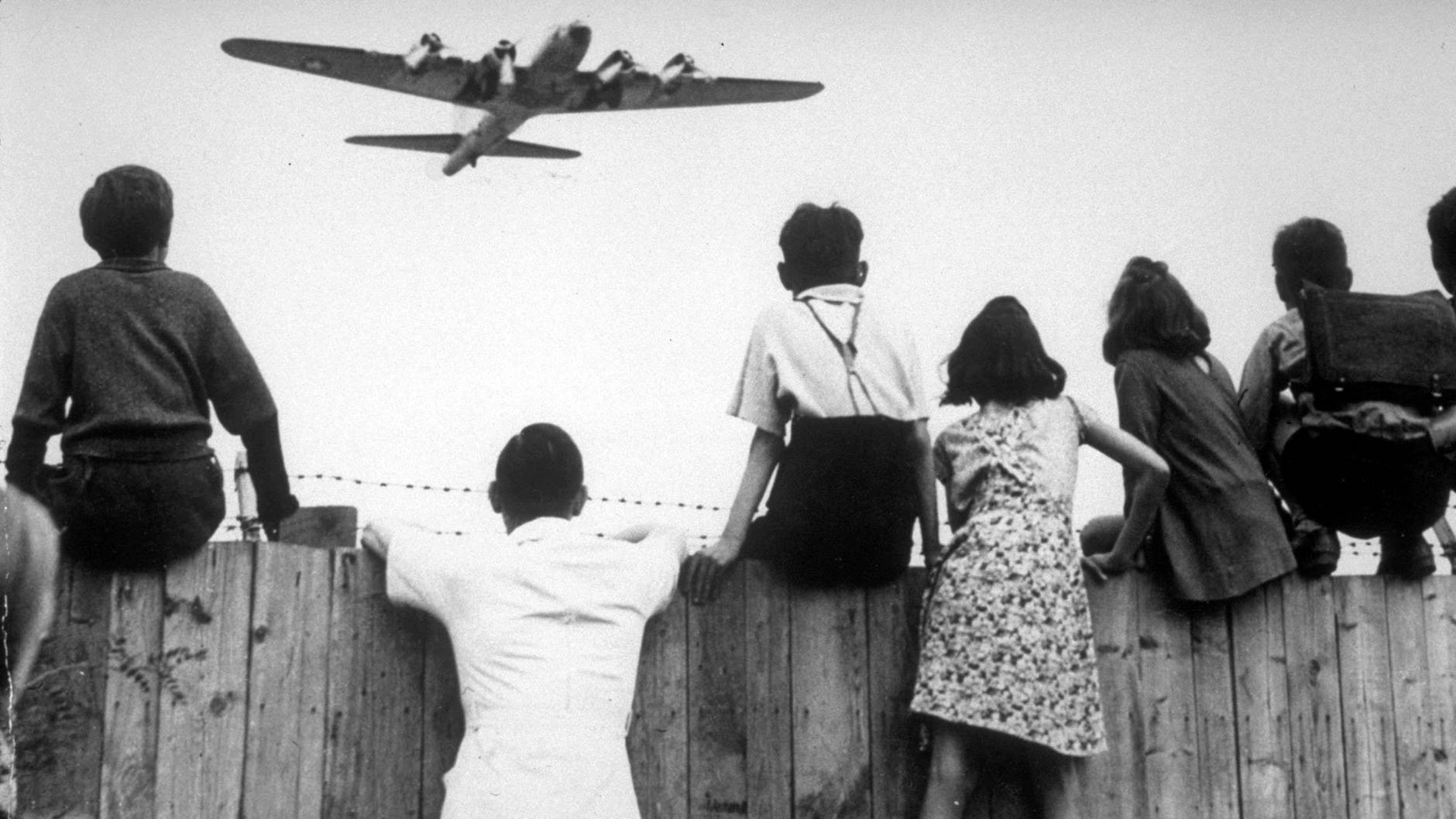 Berliner Kinder sitzen 1948 auf dem Zaun des Berliner Flughafens Tempelhof, während ein Bomber der US-Luftstreitkräfte zur Landung ansetzt.&nbsp;