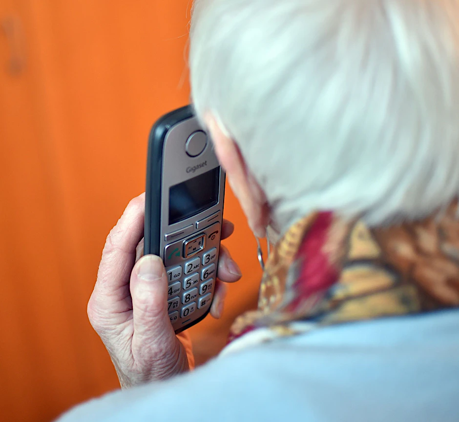 Eine Seniorin hält einen Telefonhörer an ihr Ohr.