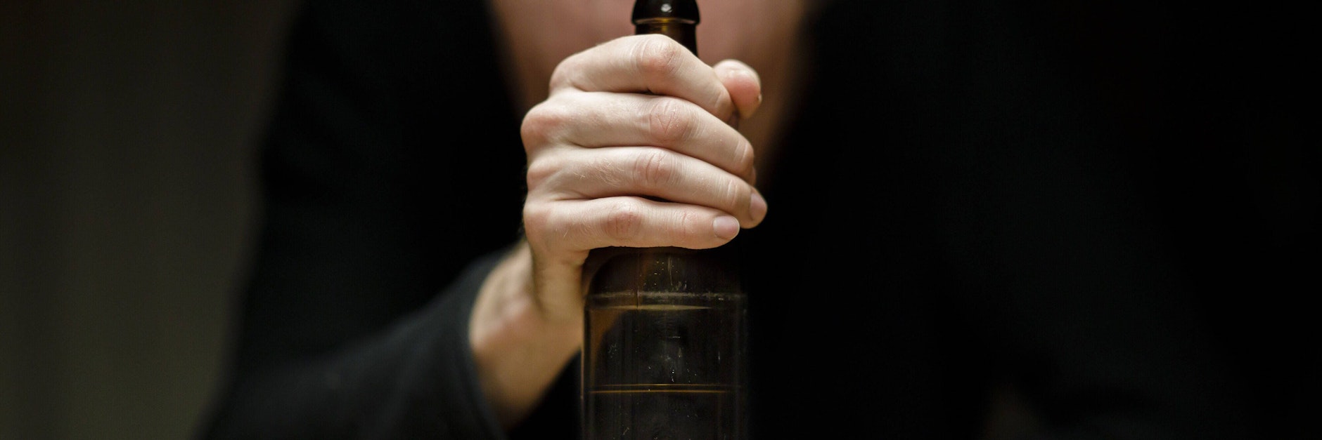 Ein Mann sitzt allein zu Hause an einem Tisch und hält eine Flasche Bier in der Hand.&nbsp;