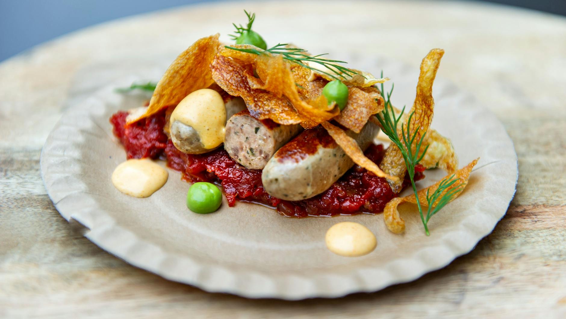 Wurst aus Wild: Die Bratwurst mit Tomaten-Chutney und grüner Chili-Mayo. Als Garnitur: knusprig frittierte, hauchdünne Kartoffelschalen.<br><br><br>