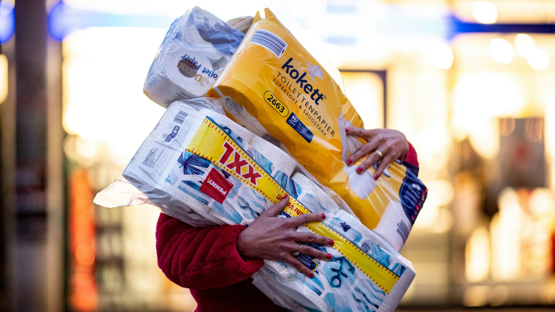 Ein Frau läuft mit dem Arm voller Klopapierrollen aus einem Drogeriemarkt heraus. Inzwischen sind die Regale doch wieder gut gefüllt.