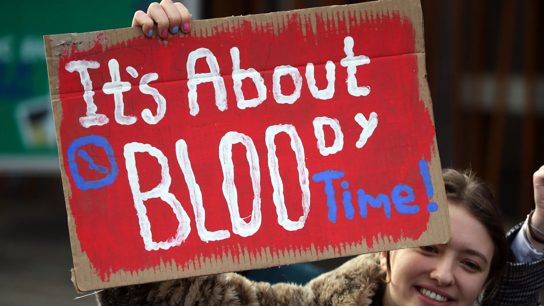 Eine Frau hält bei einer Kundgebung ein Schild mit der Aufschrift „It’s about bloody time!“.