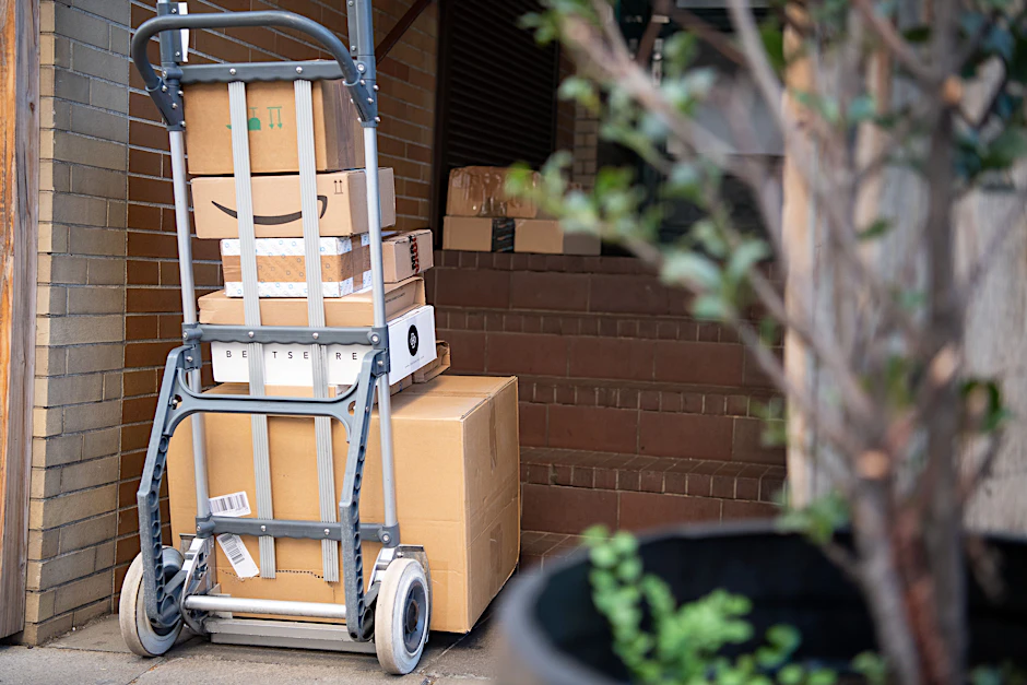 Pakete stehen auf einer Karre, während ein Paketzusteller Pakete ausliefert.