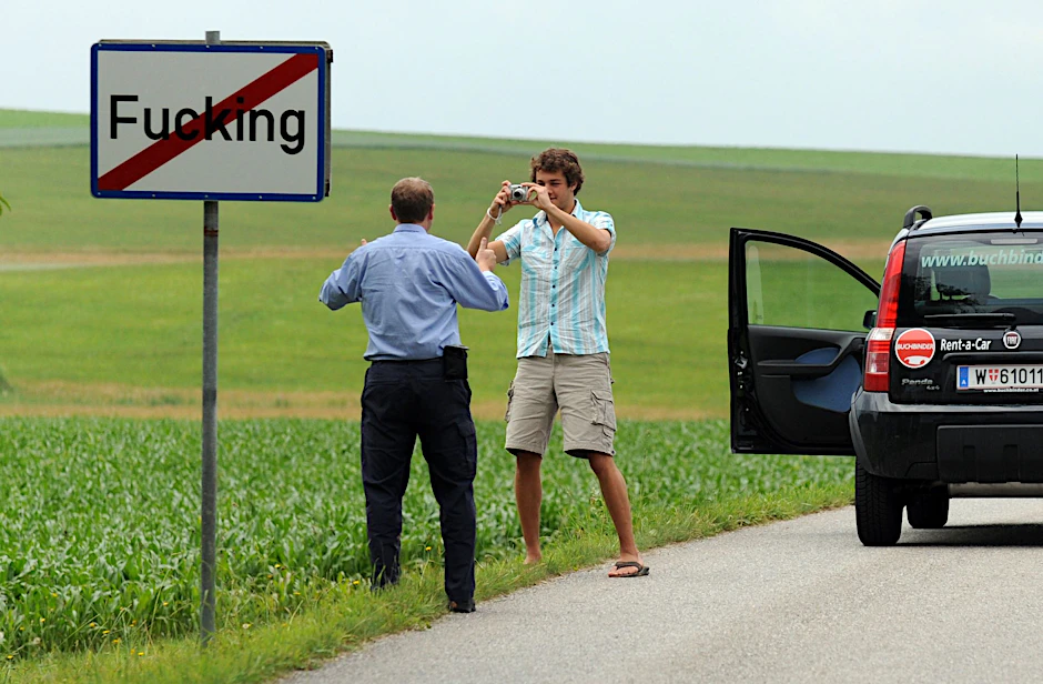 Touristen machen am Ortsschild von Fucking ein Foto.