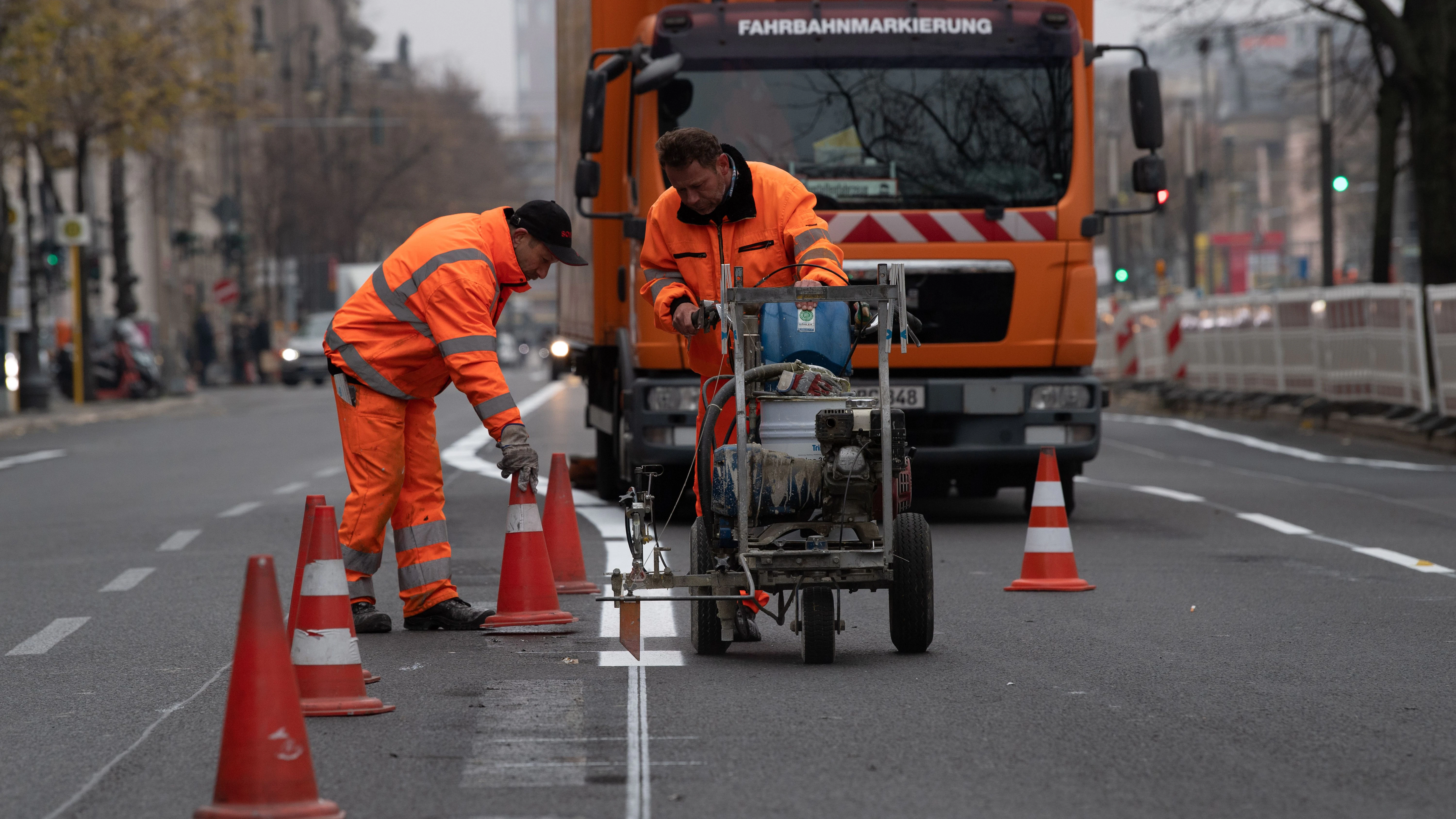 Arbeiter zeichnen neue Fahrspuren auf der Straße Unter den Linden. Nach dem Abbau der Baustelle für die neue U-Bahnlinie U5 vom Roten Rathaus bis zum Brandenburger Tor führen die Fachleute Markierungsarbeiten durch.