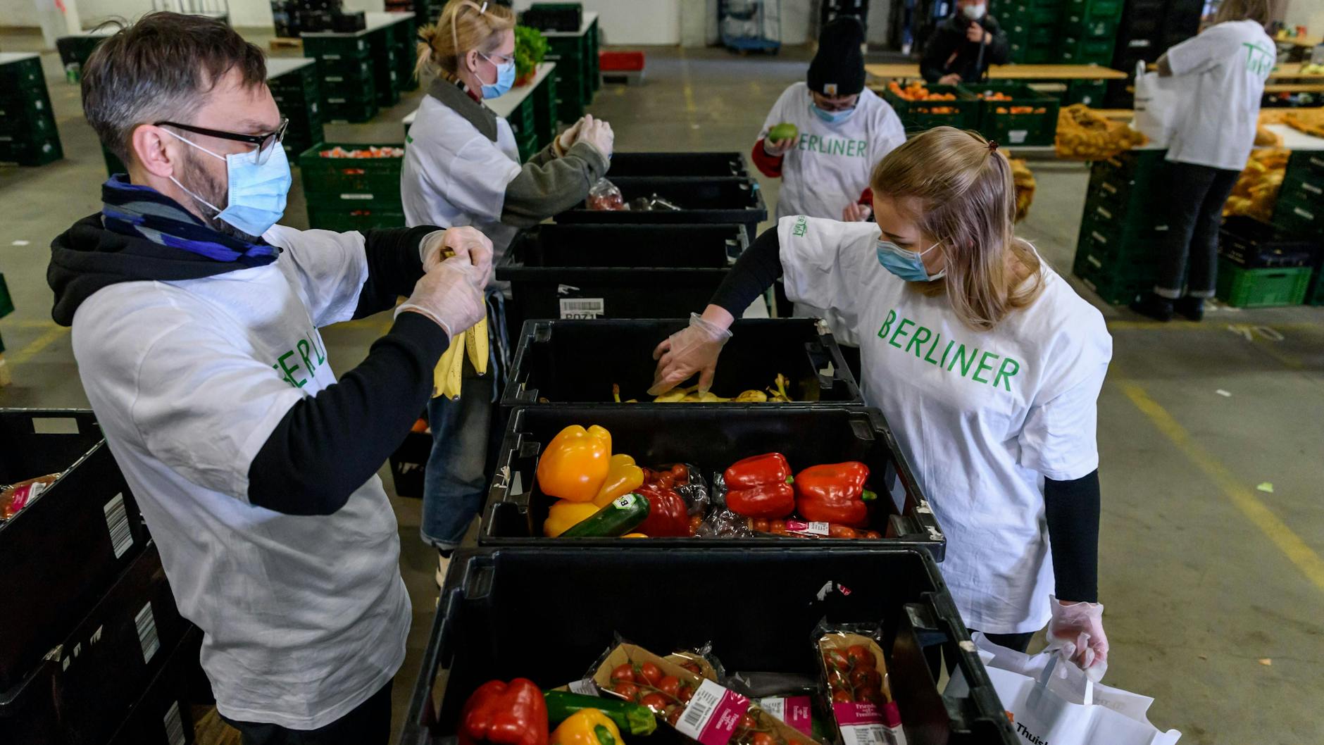 In einer Halle des Berliner Großmarkts packen ehrenamtliche Helfer der Berliner Tafel Lebensmittel in Tüten.