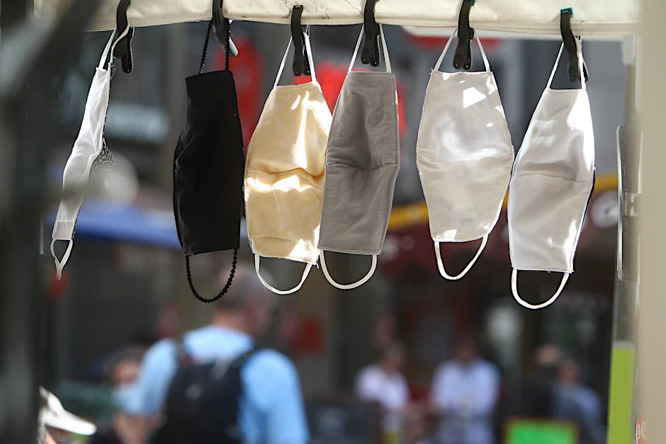 Modische Mund- Nasen Masken aus Biobaumwolle, hergestellt in handwerklicher Näharbeit, hängen an einem Marktstand.